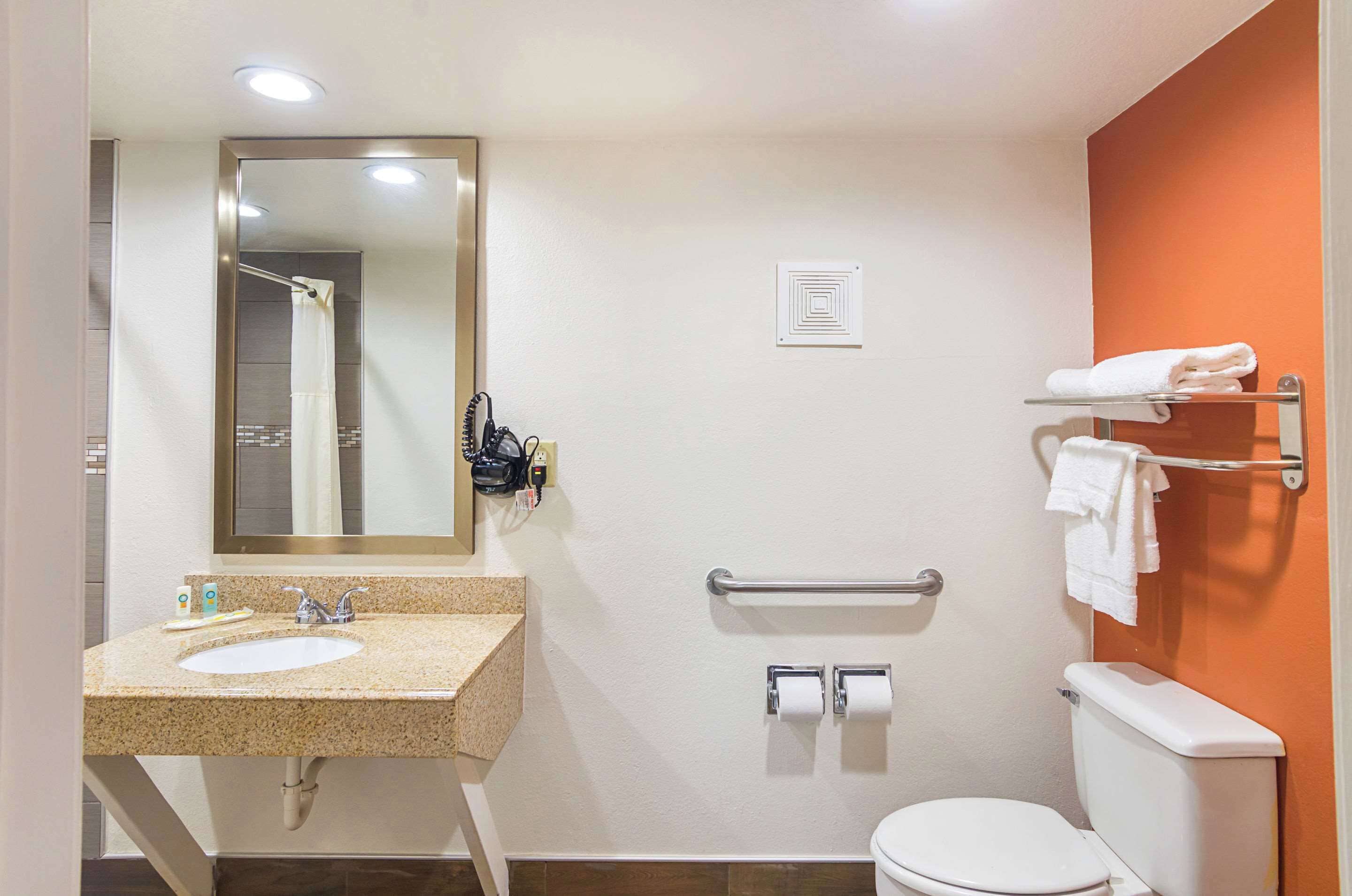 Een badkamer met een wastafel, spiegel, handdoekrek, toilet en handgrepen.