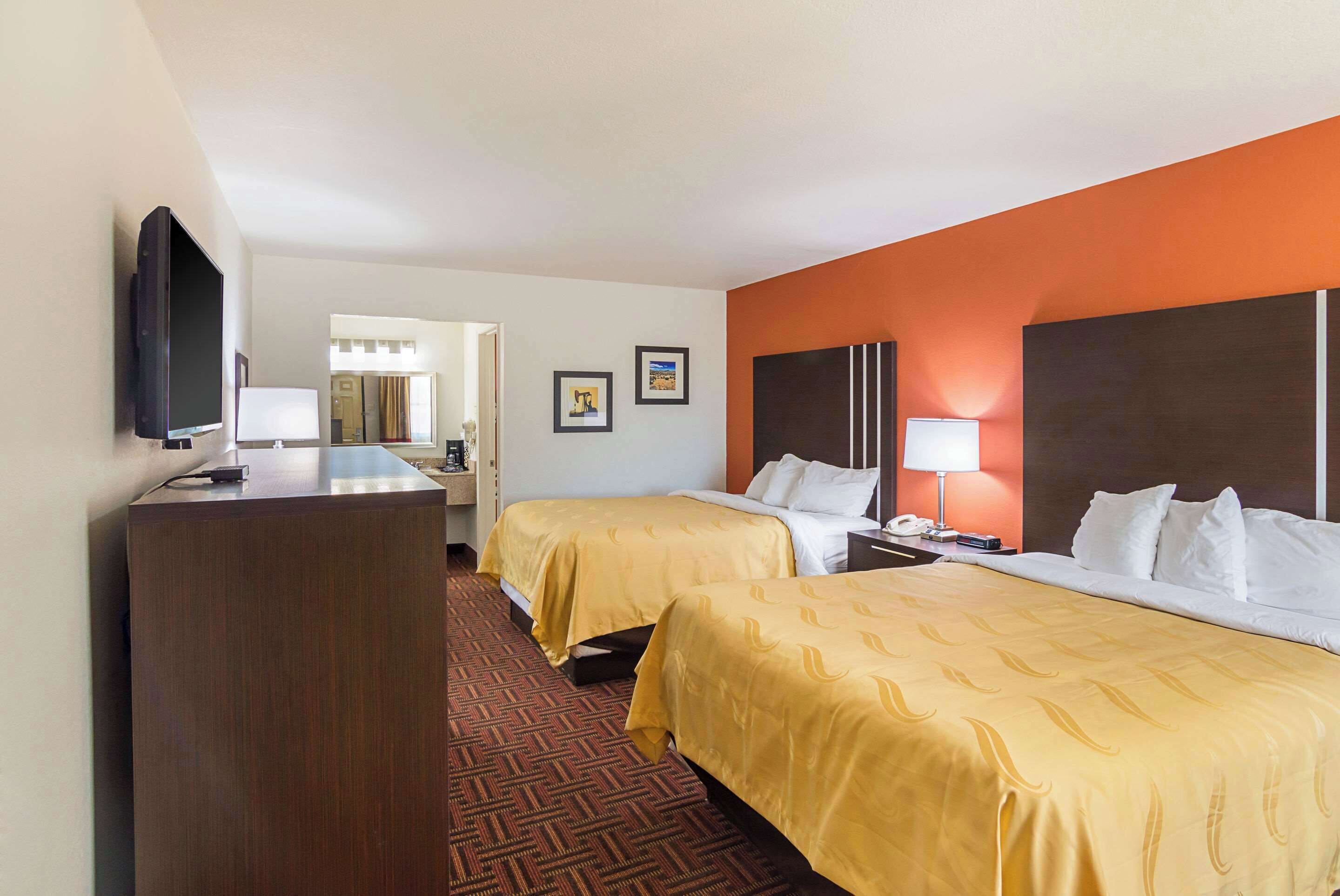 A hotel room with two beds, a desk, a television, and a bathroom visible through an open door.