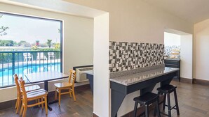 Une cuisine moderne avec un mur recouvert de carreaux, un coin repas avec des chaises en bois et une vue sur une piscine à travers de grandes fenêtres.