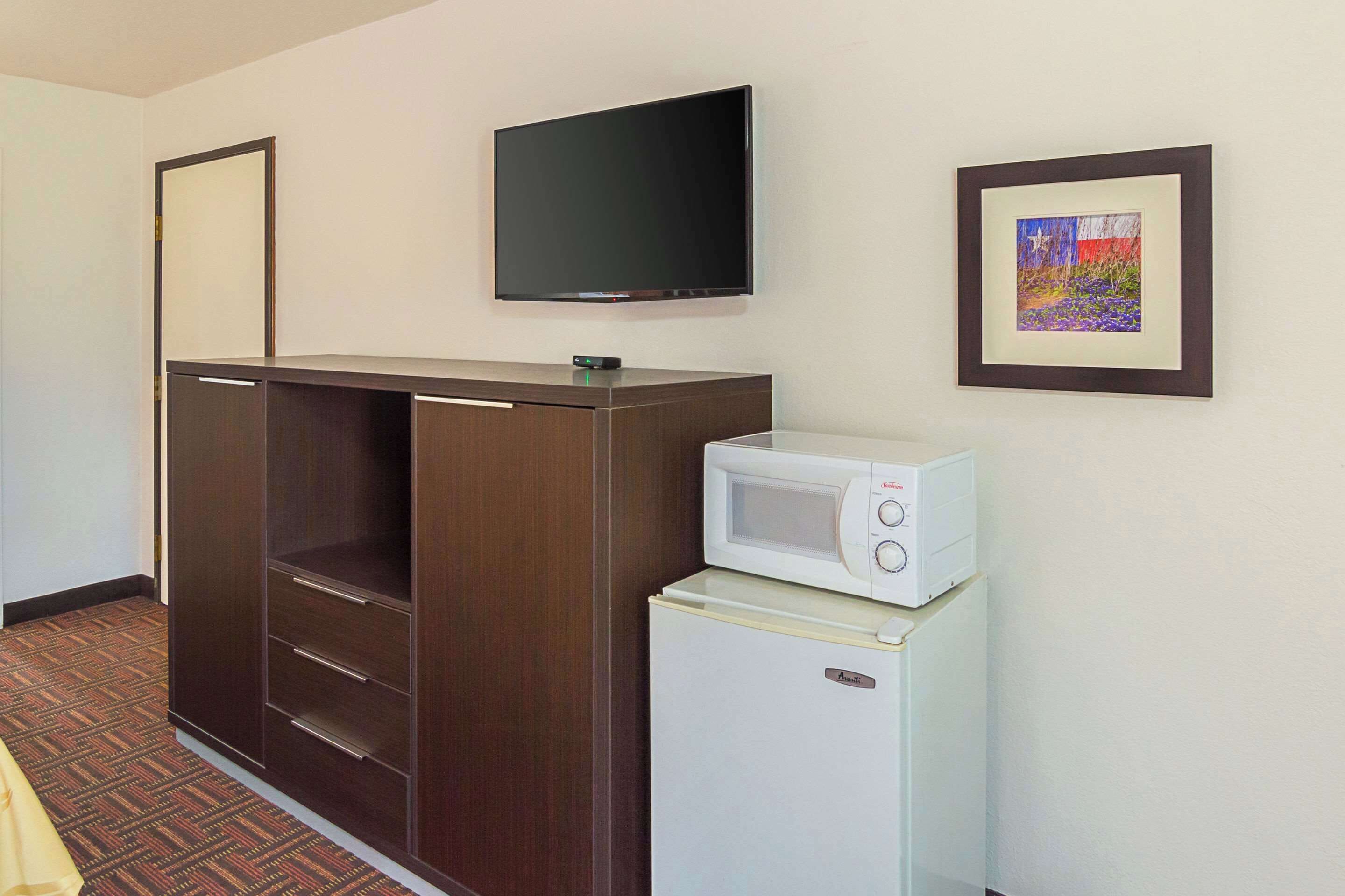 Una habitación con armario, televisión de pantalla plana, un cuadro enmarcado y un microondas sobre un refrigerador pequeño.