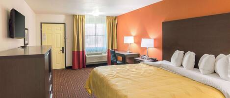 A hotel room with a bed, a desk, a chair, a television, and a door.