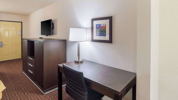 A hotel room with a desk, chair, TV, lamp, and artwork on the wall. - Quality Inn Amarillo East (Amarillo)
