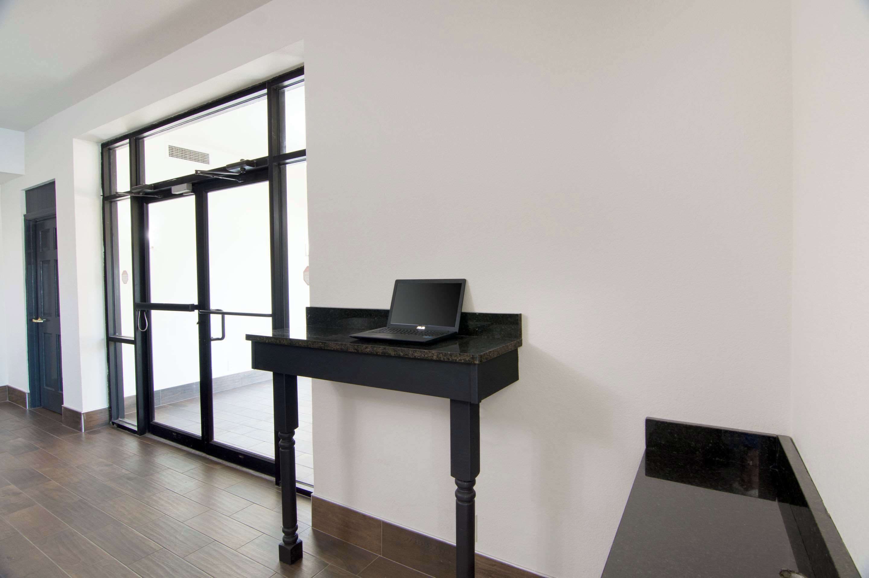 A modern interior with a black desk and laptop, a glass door entrance, and a wooden floor.