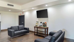 Un salon moderne avec deux canapés en cuir noir, une table basse en bois et un téléviseur à écran plat fixé au mur.