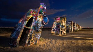 Une rangée de bâtiments à l’architecture originale, décorés de graffitis, peut-être à des fins artistiques ou culturelles, se dressant sur fond de ciel nocturne.