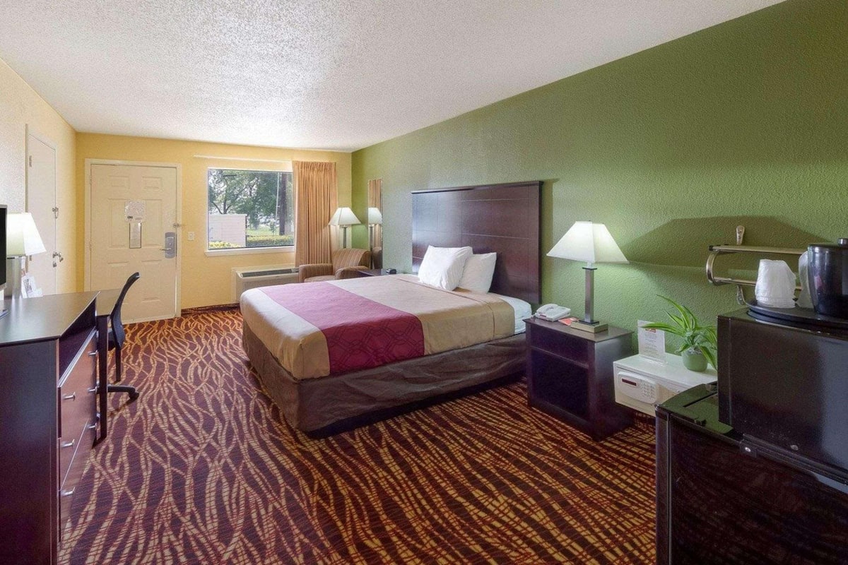 Una habitación de hotel con cama, escritorio, silla, mesitas de noche, lámparas y televisión.
