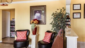 Un espace d’accueil comprenant deux fauteuils en cuir noir, un vase avec des fleurs, un tableau encadré au mur et une plante.