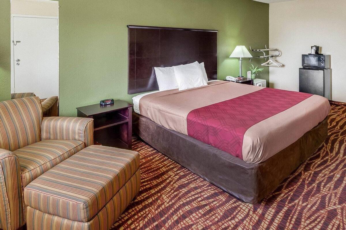 Une chambre d’hôtel avec un lit, une chaise, une table de chevet, une lampe et un petit téléviseur.