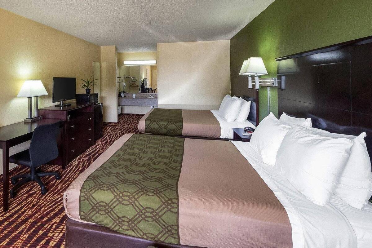 Une chambre d’hôtel avec deux lits, un bureau, une chaise, une télévision et un miroir.