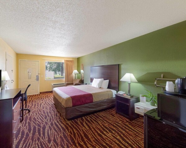 A hotel room with a bed, bedside tables, a desk, a chair, a TV, and a window.
