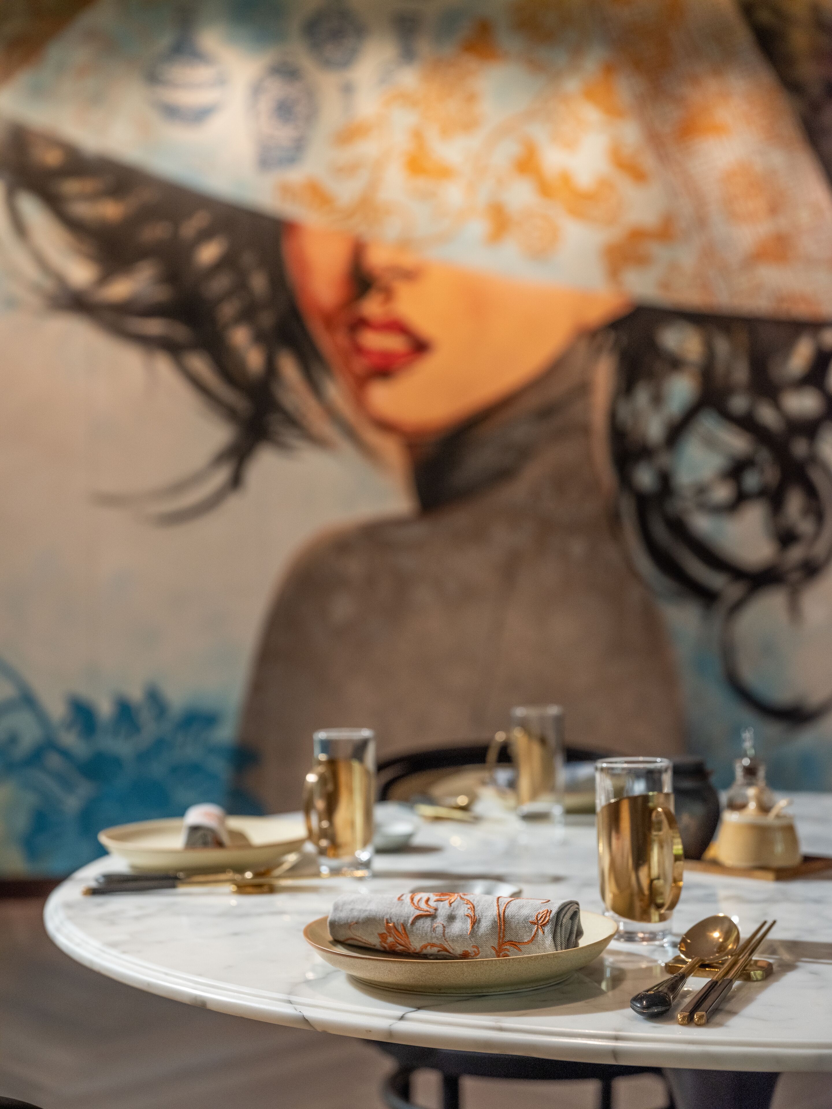 Una mesa de comedor dispuesta con platos, vasos y cubiertos, con un cuadro al fondo.