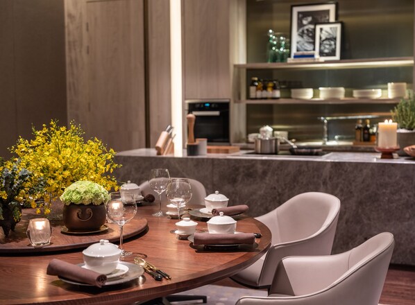 Un comedor con una mesa de madera dispuesta para dos personas, con vajilla blanca, vasos y un jarrón con flores amarillas.