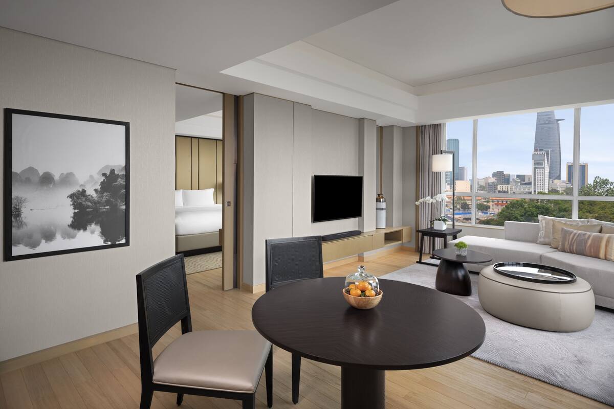 Een moderne hotelkamer met uitzicht op de stad, een eethoek en een slaapkamer met een groot bed en een flatscreen-tv.