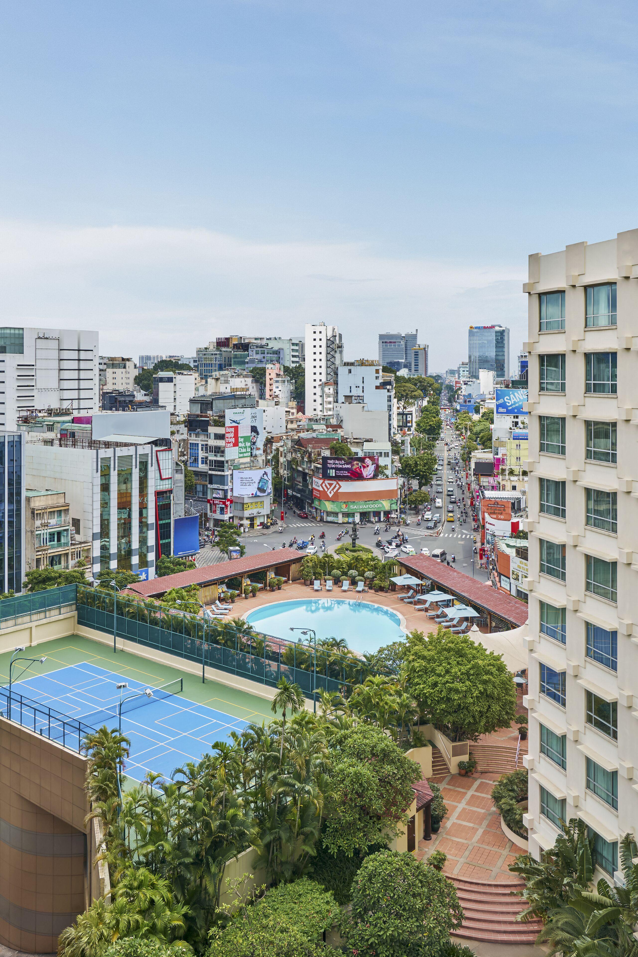 A high-rise building with a rooftop pool surrounded by greenery and a tennis court.