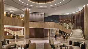 Un hall d’entrée spacieux avec un escalier central, des coins salon et un lustre moderne.