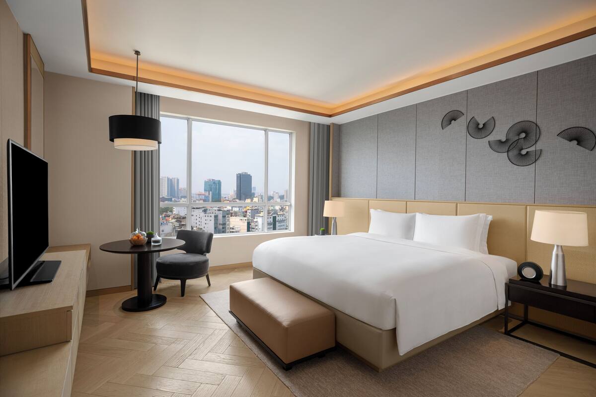Een moderne hotelkamer met een groot bed, een televisie, een bureau en uitzicht op de stad.