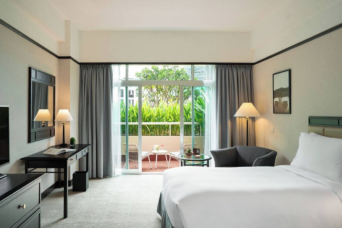 Een hotelkamer met een bed, bureau, stoel en een balkon met gordijnen.