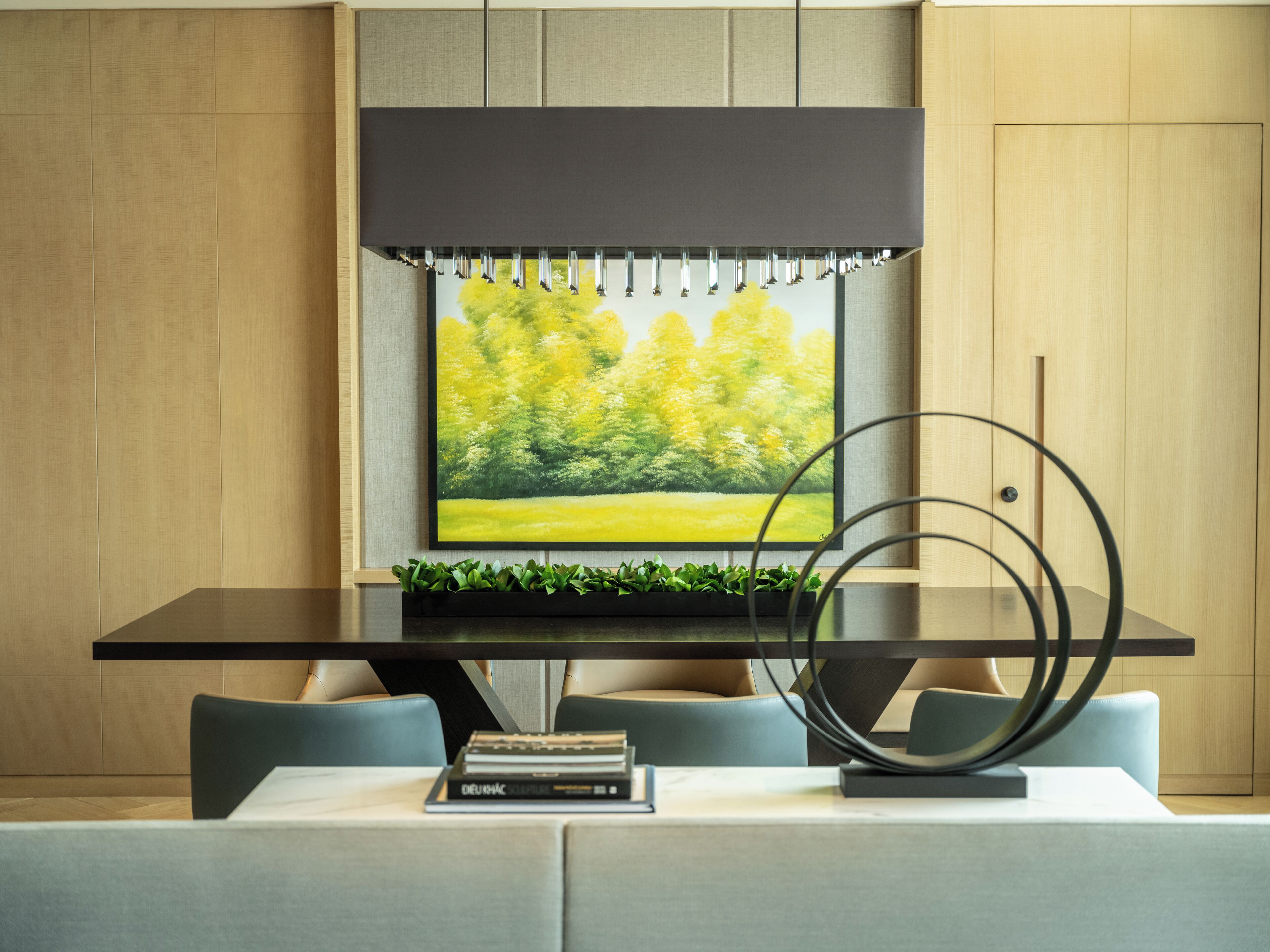 Un área de comedor moderna con una mesa negra, sillas tapizadas en gris, un cuadro de un paisaje verde y una escultura de metal decorativa.
