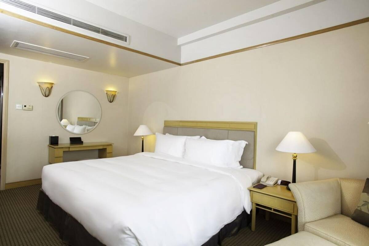 Een hotelkamer met een groot bed, bedlampen, een bureau met lamp, een stoel en een ronde spiegel aan de muur.