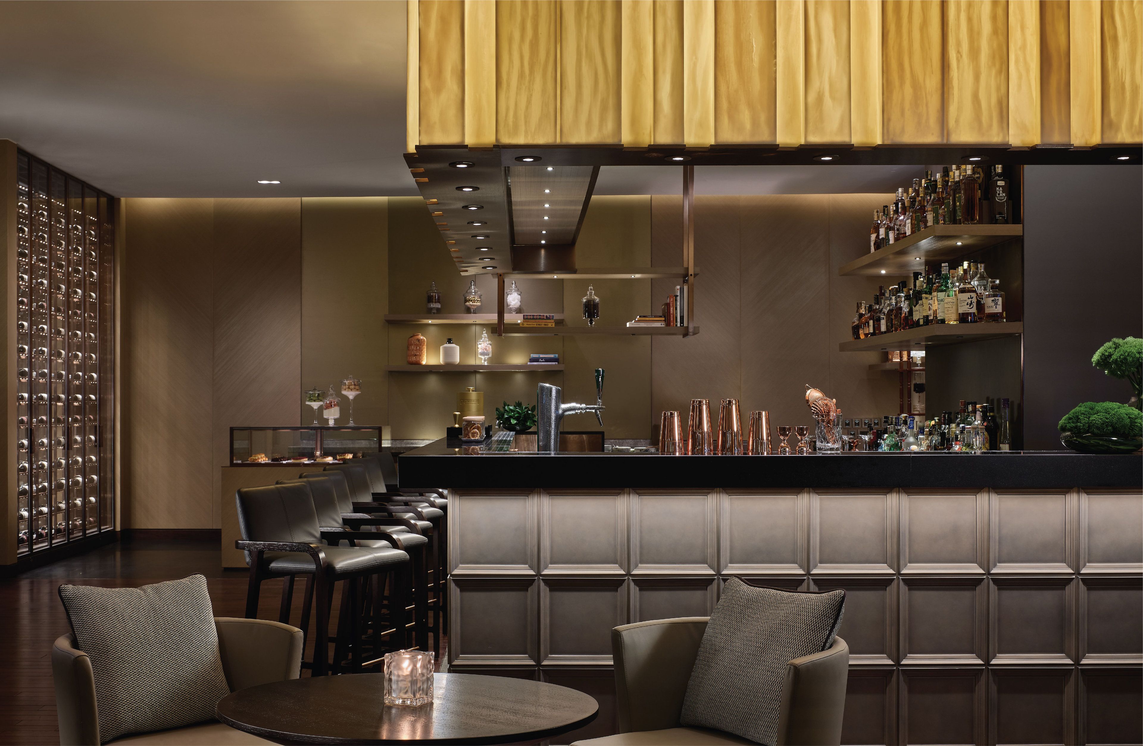 Een bar met zitplaatsen, een toonbank vol flessen en een decoratieve wand.