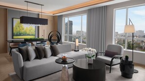 Un salon moderne avec un canapé gris, une table basse ronde et une vue sur la ville grâce à de grandes fenêtres.
