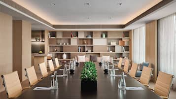 A conference room with a long table, chairs, and shelves with books and decorative items.