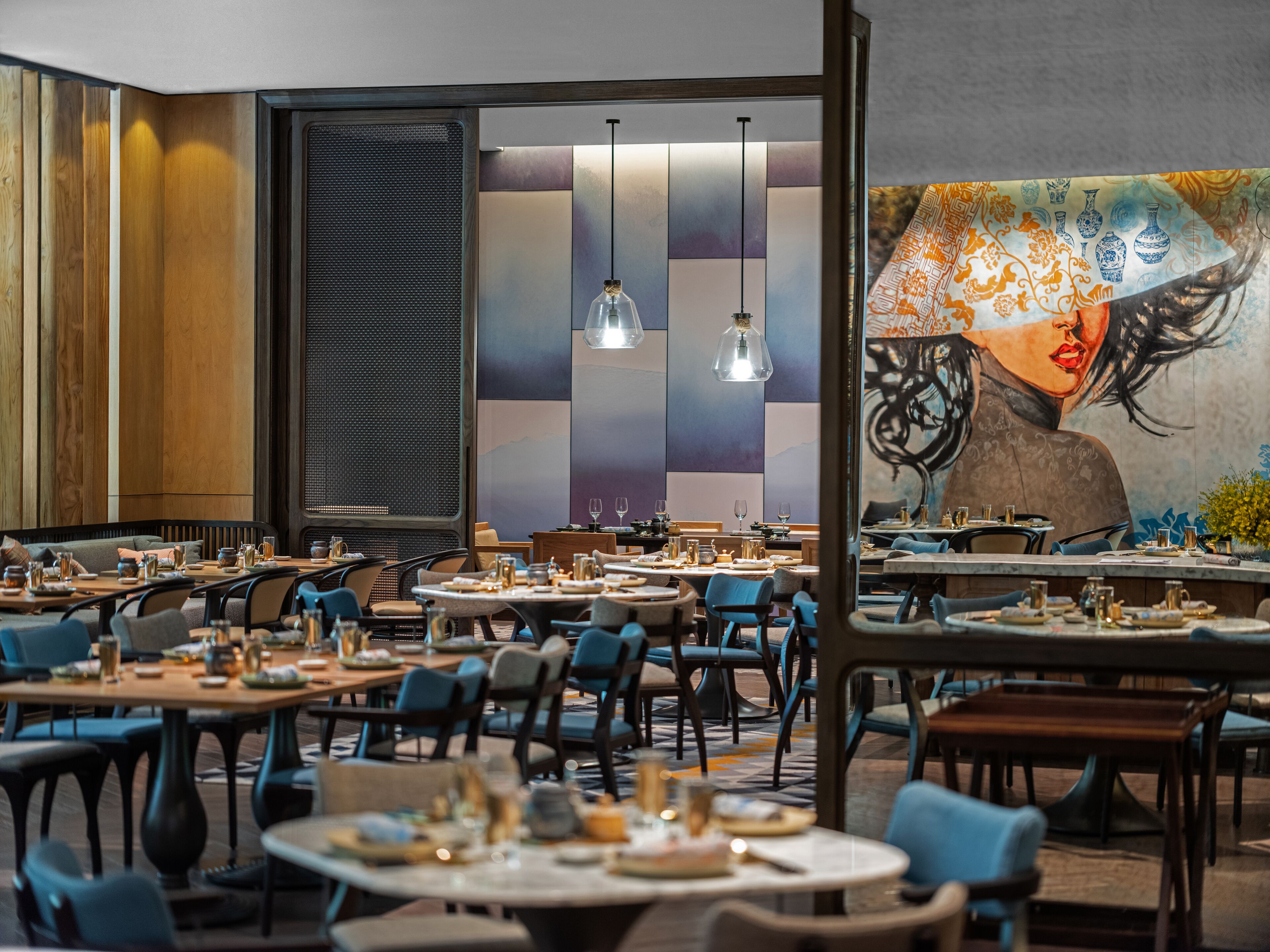 Un restaurante con varias mesas y sillas, un mural grande en la pared e iluminación colgante.