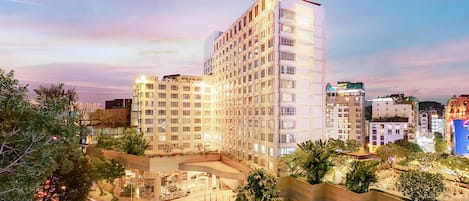 A multi-story hotel with a modern design, featuring balconies and a central courtyard with plants.