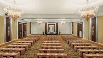 Un salón de conferencias con filas de mesas, candelabros y una pantalla grande al frente.
