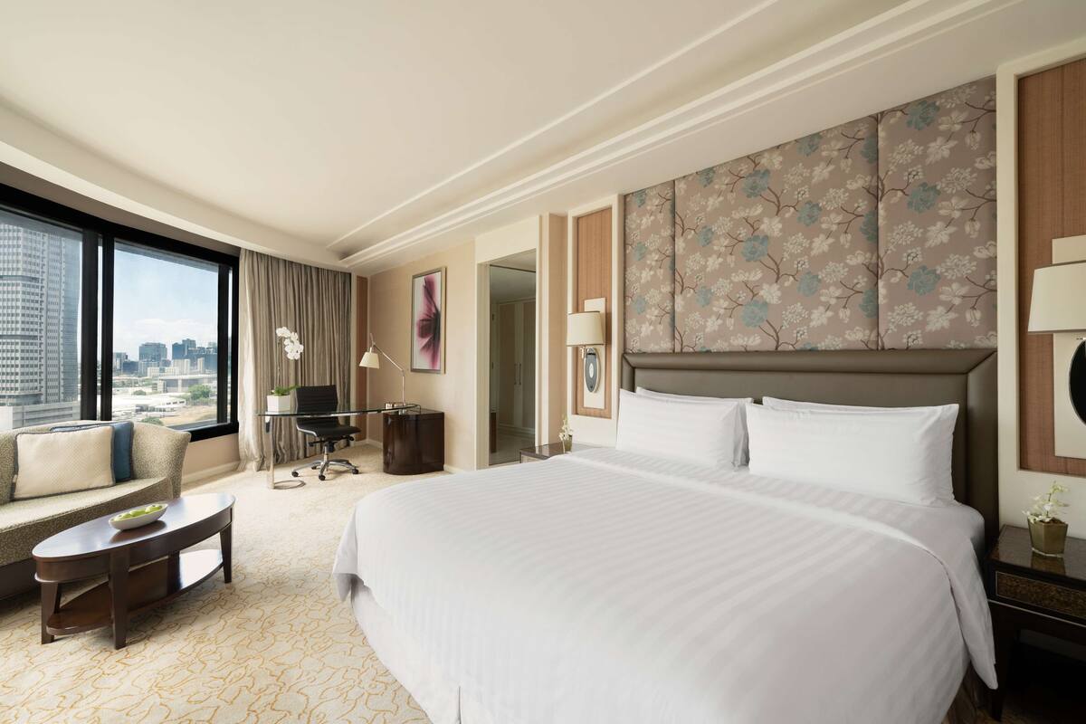 A hotel room with a large bed, a sofa, a desk, and a view of the city.