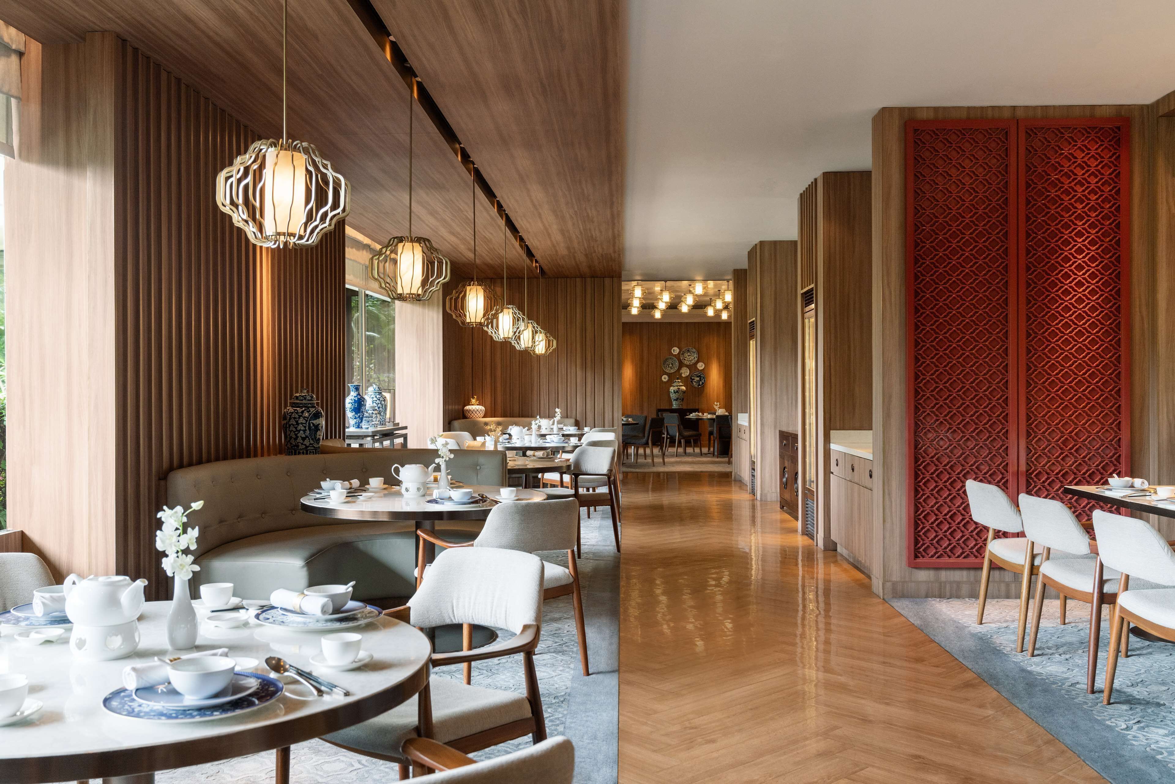 Uma sala de jantar moderna com painéis de madeira, mesas redondas e luminárias pendentes.