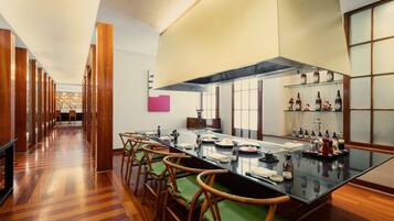 A modern kitchen with a long dining table, wooden chairs, and a variety of bottles on shelves.