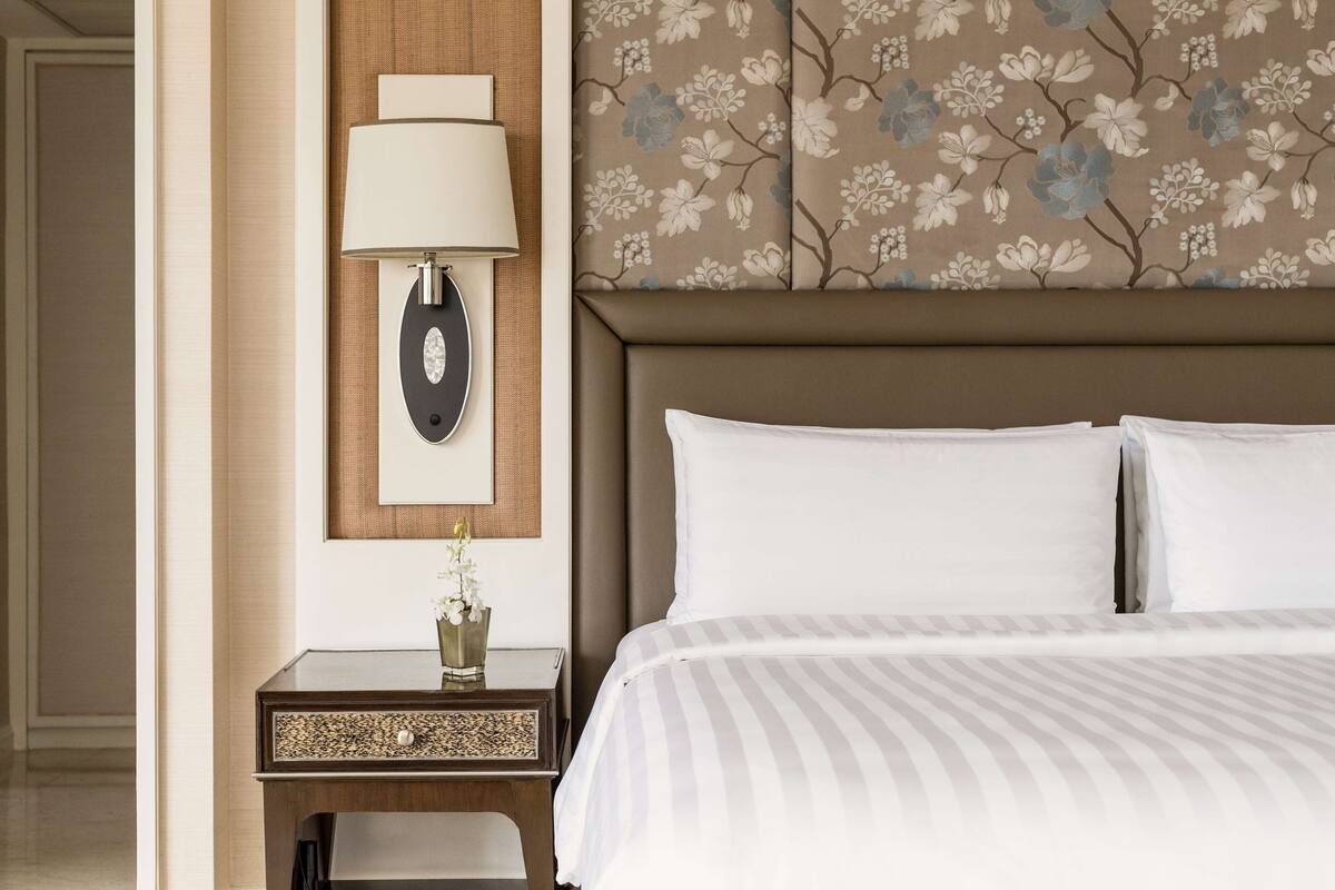 A hotel room with a bed, a nightstand with a lamp, and a floral-patterned wall.