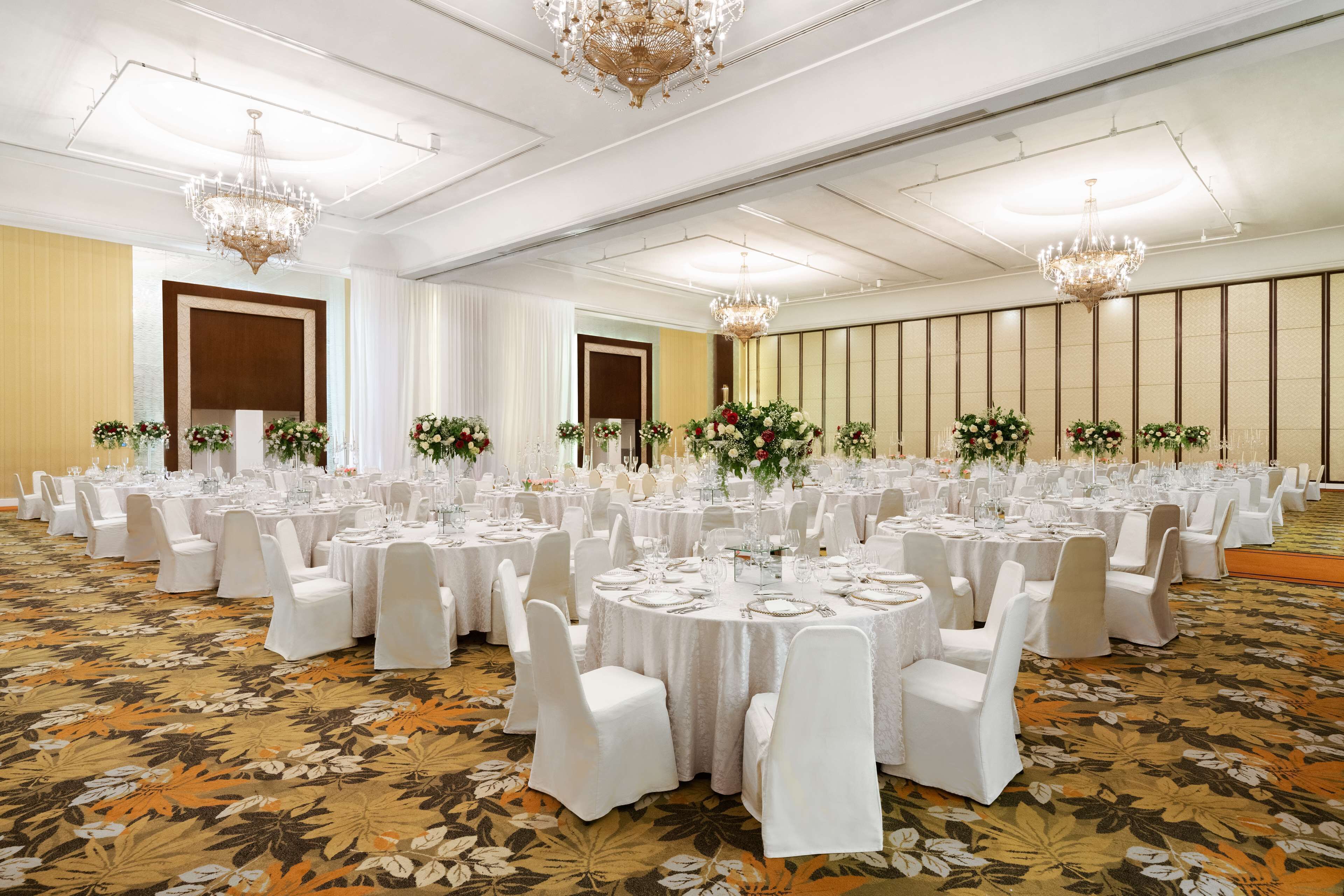 A banquet hall with round tables, white chairs, and floral centerpieces.