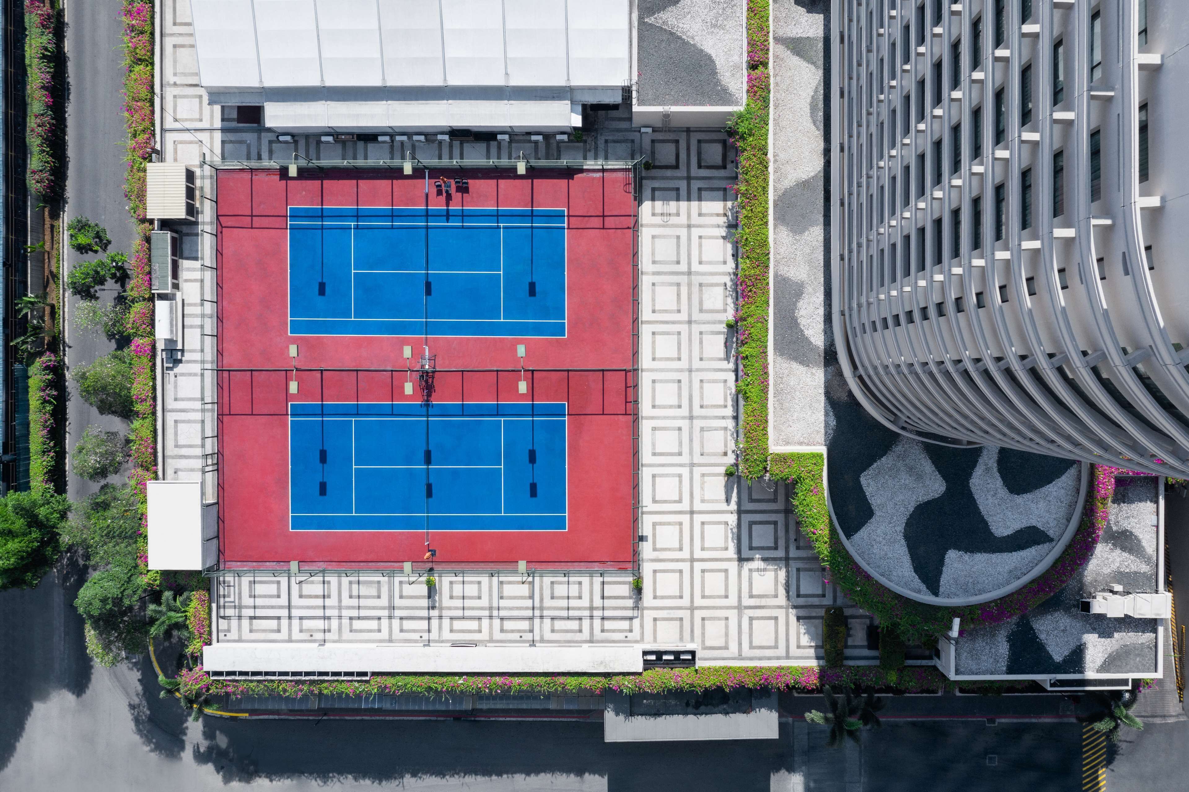 An aerial view of a tennis court with a red and blue surface, surrounded by a white building with a curved facade.