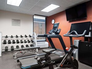 Een fitnessruimte met loopbanden, elliptische trainers en gewichten.