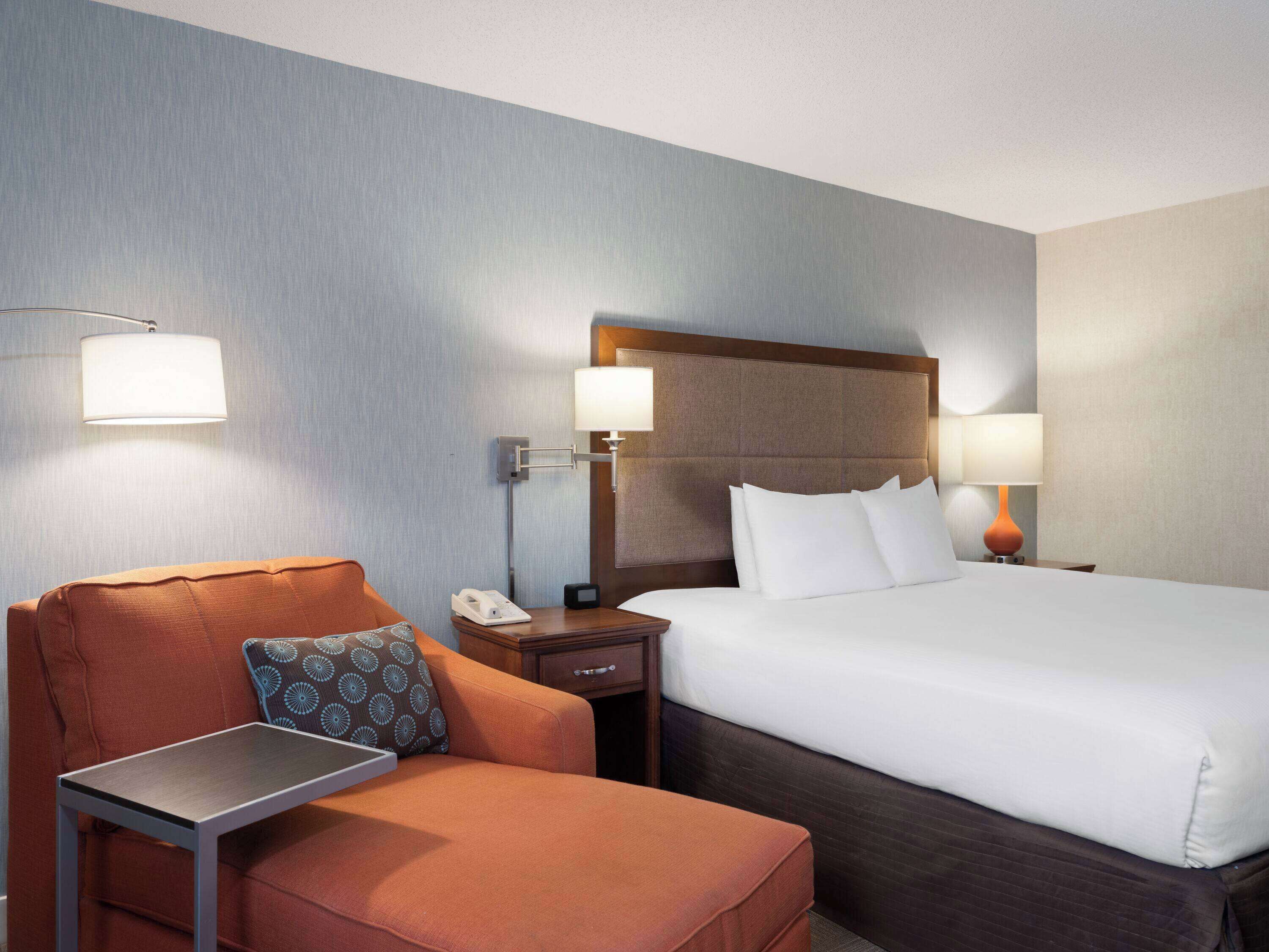 Ein Hotelzimmer mit einem Bett, einem Sessel, einem Nachttisch und einem Schreibtisch.