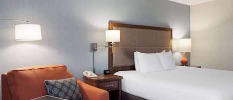 Una habitación de hotel con cama, una silla, una mesita de noche y un escritorio.