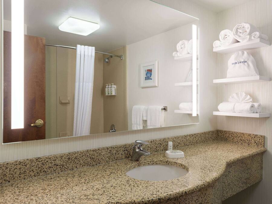 A bathroom with a granite countertop sink, a mirror, a shower with a glass door, and shelves with neatly folded towels.