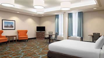 A hotel room with a large bed, two armchairs, a TV, a small table, and a window with curtains.
