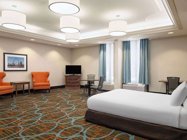A hotel room with a large bed, two armchairs, a TV, a small table, and a window with curtains. - Wingate by Wyndham St. Louis Airport (St. Ann)