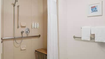 Een badkamer met douche, handgrepen, een klein tafeltje, toilet en handdoekhouder.