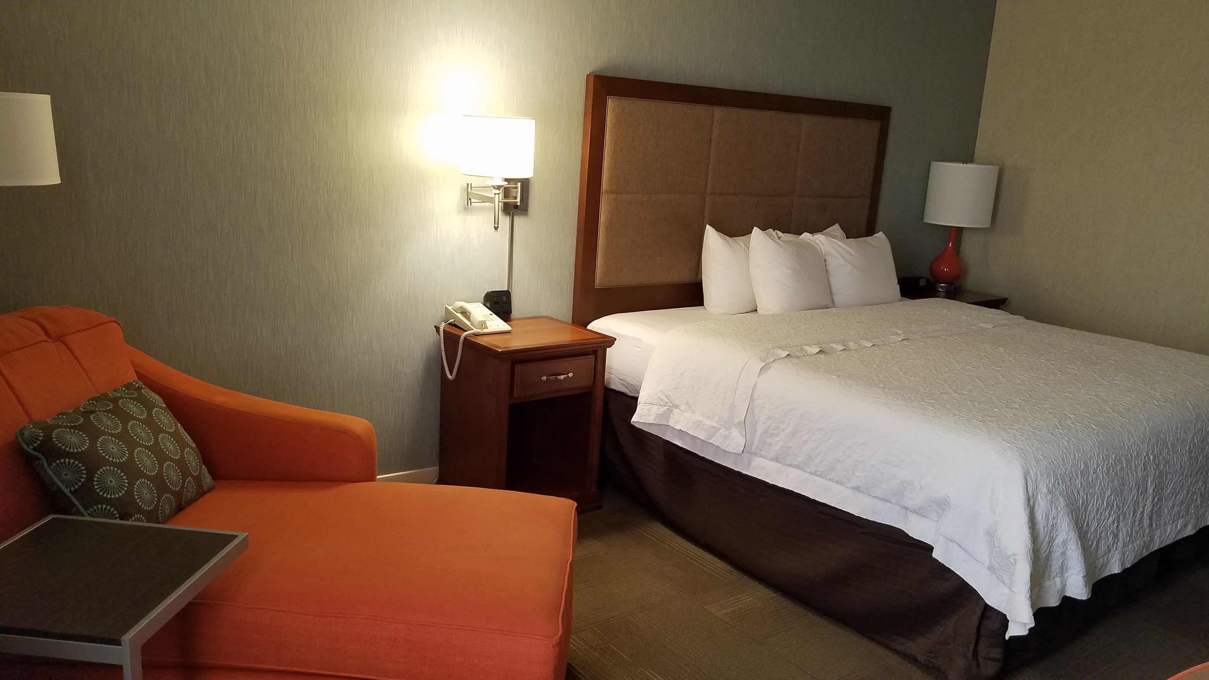 Una habitación de hotel con una cama, un escritorio, una silla y una mesita de noche con una lámpara.