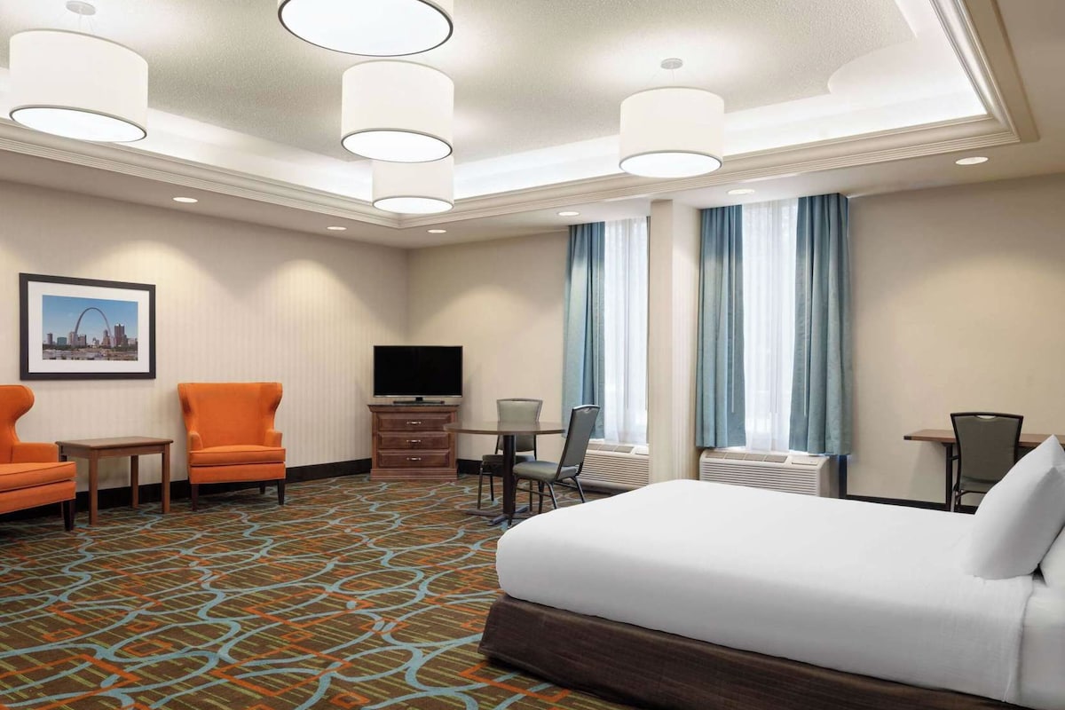 Une chambre d’hôtel avec un grand lit, deux fauteuils, une télévision, une commode et une petite table.