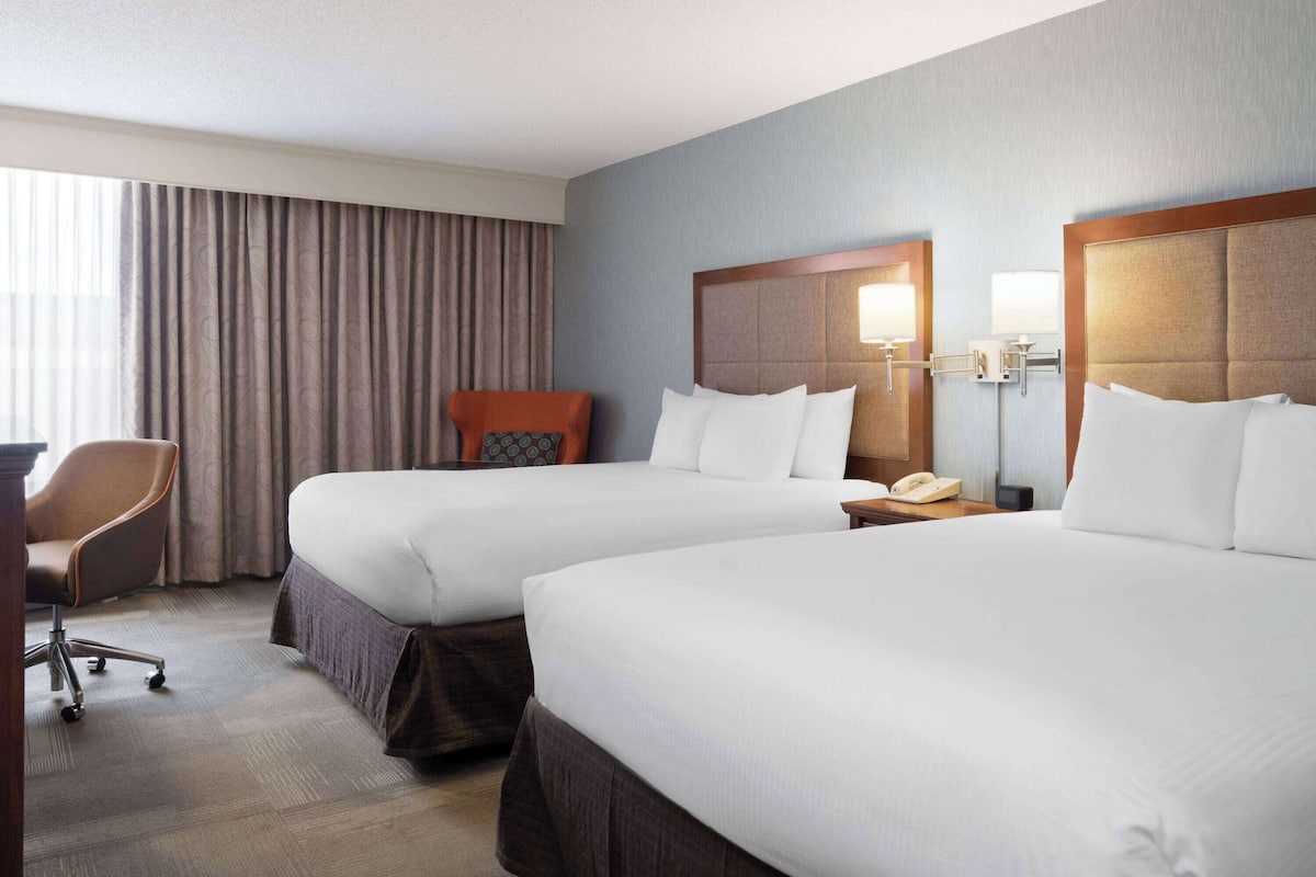 A hotel room with two beds, a desk, and a chair.