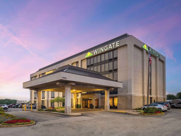 Un hotel Wingate con entrada cubierta, estacionamiento y una bandera.