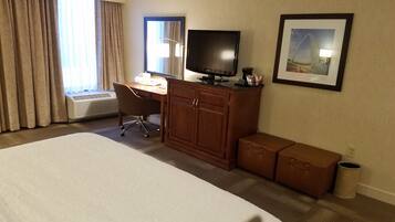 A hotel room with a large bed, a desk with a computer, a television, and a framed picture on the wall.