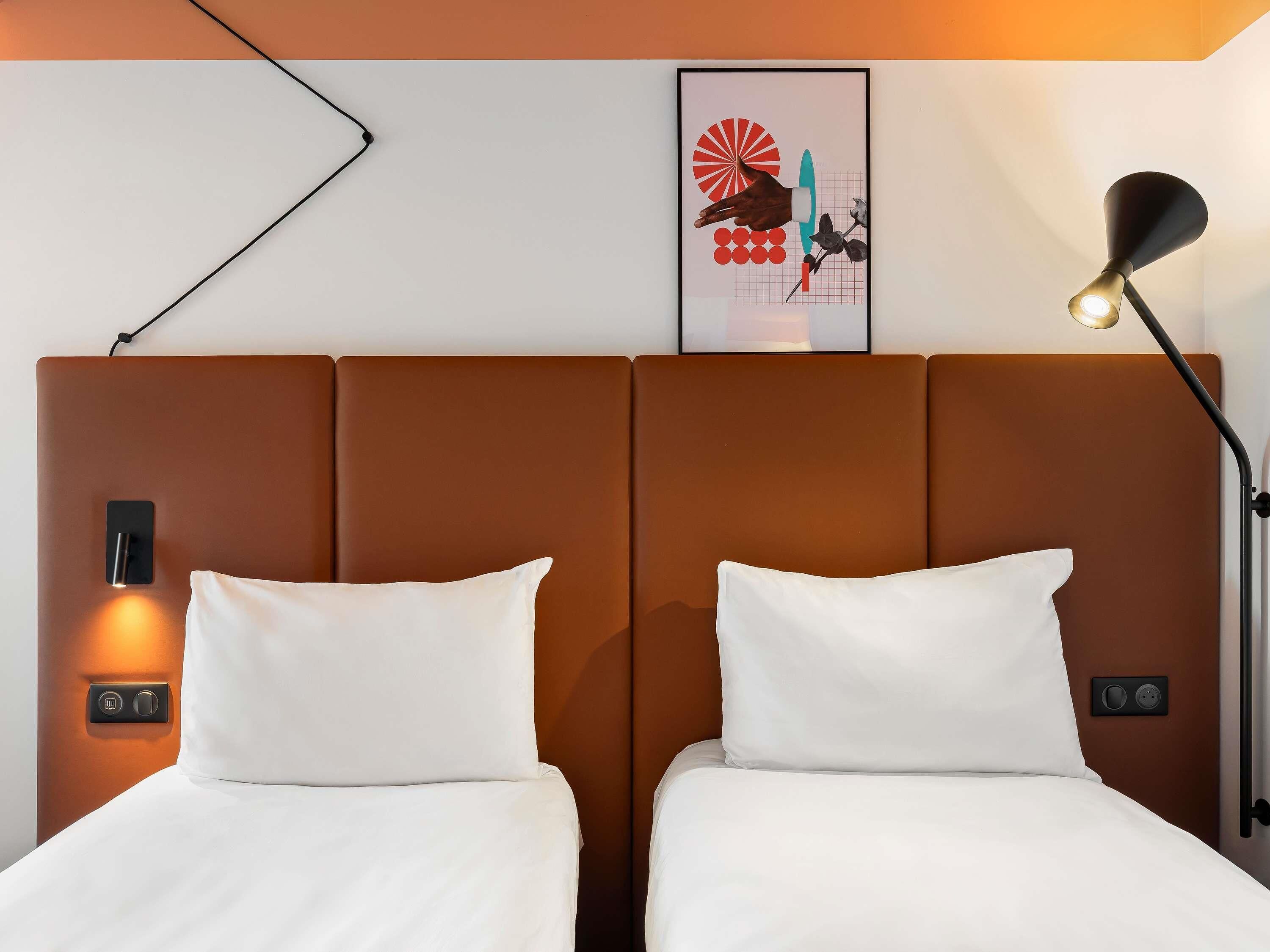 A hotel room with two beds, a wall-mounted artwork, a bedside lamp, and a control panel.