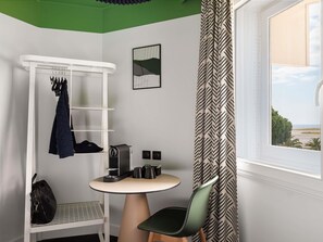 A compact room with a white ceiling, a window with a view, a white shelf with hanging clothes, a small table with a coffee machine, and a chair. - ibis Nice Aéroport Promenade des Anglais (Nice)