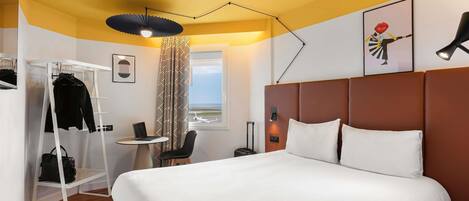 A hotel room with a bed, a desk, a chair, a wardrobe, and a window with an airplane view.